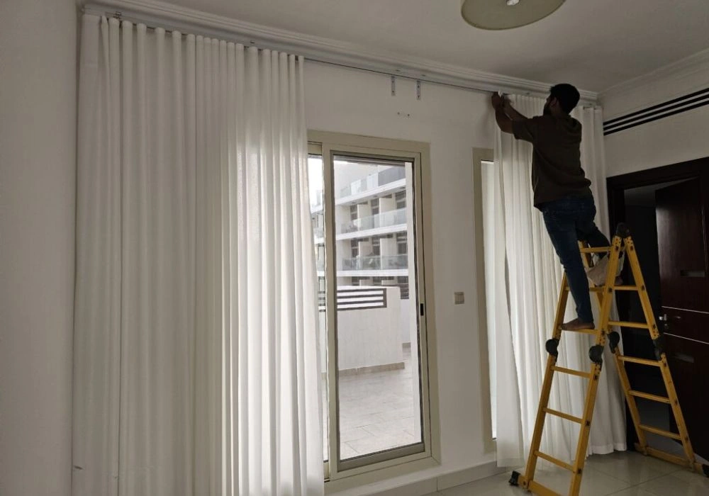 Worker fixing white tracks curtain installation