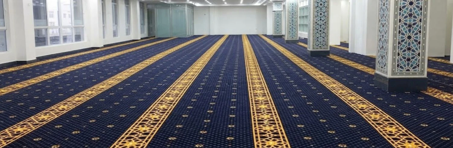 Deep blue and gold patterned mosque carpet rolls in large hall